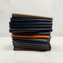 Load image into Gallery viewer, Franklin-Christoph stack of 5.3 pocket notebook covers in various colors and materials including black leather, brown, navy, grey, and orange.