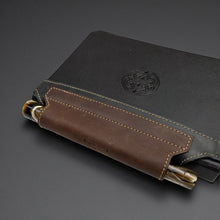 Load image into Gallery viewer, Franklin-Christoph black and brown leather elastic pen holder with creme stitching attached to a black notebook.